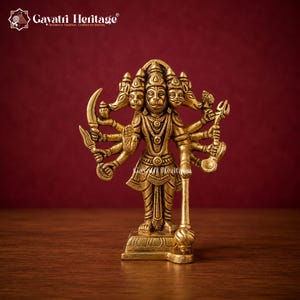 May include: A brass-colored metal statue of a five-headed deity with ten arms, standing on a rectangular base. The figure holds various symbolic items including a mace, a sword, and a trident. The text Gayatri Heritage is visible at the top.