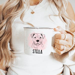 Puede incluir: Taza de esmalte blanco con un dibujo lineal de la cara de un perro y un fondo rosa de acuarela. El nombre "STELLA" est&aacute; impreso en negro debajo de la ilustraci&oacute;n del perro. La taza tiene un acabado moteado.