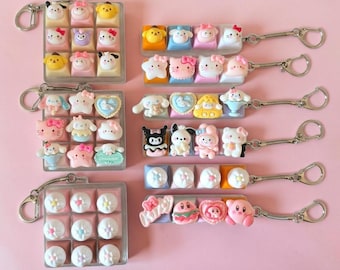May include: A collection of keychains featuring miniature character figures and decorative shapes attached to square or rectangular bases. The designs include various colourful cartoon-inspired motifs, pastel-coloured accents, and metallic rings.