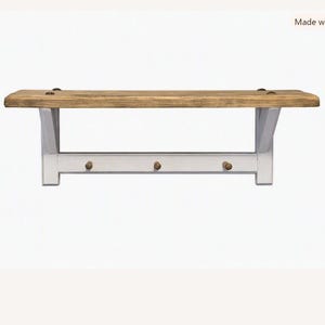 May include: A wall-mounted shelf featuring a natural wood grain top surface supported by white metal brackets. The unit includes a horizontal white metal bar underneath the shelf, equipped with three small, round, wooden knobs for hanging items.