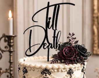 May include: A white tiered cake decorated with black piping and intricate black filigree details. A black cake topper with the text Till Death sits on top, accompanied by a cluster of dark purple and black roses and small dark berries.