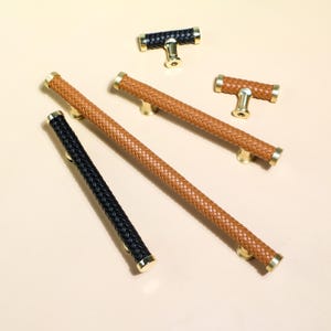 Puede incluir: Un surtido de herrajes para armarios, que incluye tiradores largos y pomos en forma de T. Los tiradores y pomos presentan un dise&ntilde;o de cuero trenzado en negro y marr&oacute;n, con detalles dorados. Los herrajes est&aacute;n dise&ntilde;ados para muebles y armarios.