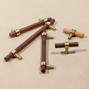 May include: A collection of wooden cabinet pulls with brass accents. The pulls are cylindrical with a dark brown finish, and the brass hardware adds a touch of elegance. Some pulls are a lighter wood tone. The hardware is a T-shape.