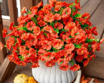 Könnte beinhalten: Eine weiße, gerippte Keramikvase, die mit leuchtend orangefarbenen Blumen mit grünen Zentren überquillt. Die Anordnung befindet sich auf einer Holzoberfläche, mit kleinen Kürbissen und Blättern in der Nähe, was ein Herbstthema suggeriert.