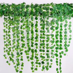 May include: Artificial green ivy garland with various leaf shapes, hanging against a white background. The garland is made of plastic and is designed for decorative purposes. The leaves vary in size and shape, creating a natural look.