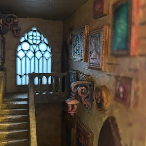 May include: A detailed miniature gothic interior diorama featuring a staircase, arched window, and framed paintings. The walls are beige, and the lighting creates a dramatic effect. The window has a blue glow.