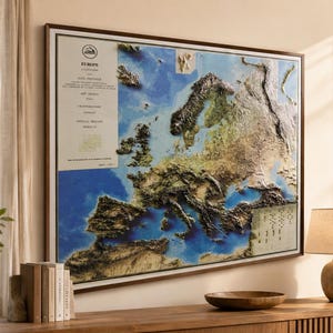 Op de afbeelding: Een ingelijste reli&euml;fkaart van Europa, met de topografie van het continent met gedetailleerde texturen en kleurvariaties. De kaart is geplaatst tegen een blauwe en bruine achtergrond, omlijst in donker hout. Een document in vintage-stijl is zichtbaar aan de linkerkant.