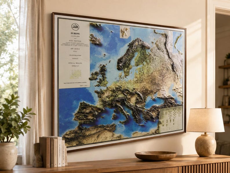 Op de afbeelding: Een ingelijste reli&euml;fkaart van Europa, met de topografie van het continent met gedetailleerde texturen en kleurvariaties. De kaart is geplaatst tegen een blauwe en bruine achtergrond, omlijst in donker hout. Een document in vintage-stijl is zichtbaar aan de linkerkant.