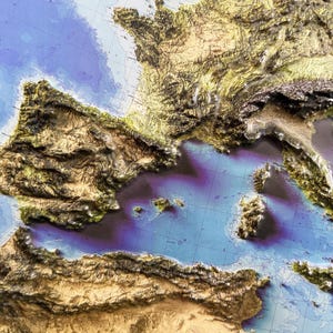 Op de afbeelding: Een 3D-reli&euml;fkaart van Europa, met de nadruk op het Iberisch schiereiland en Itali&euml;. De kaart toont gedetailleerde topografie in tinten bruin, groen en beige, met blauw dat de zee voorstelt. De kaart is een visuele weergave van de hoogte van het land.