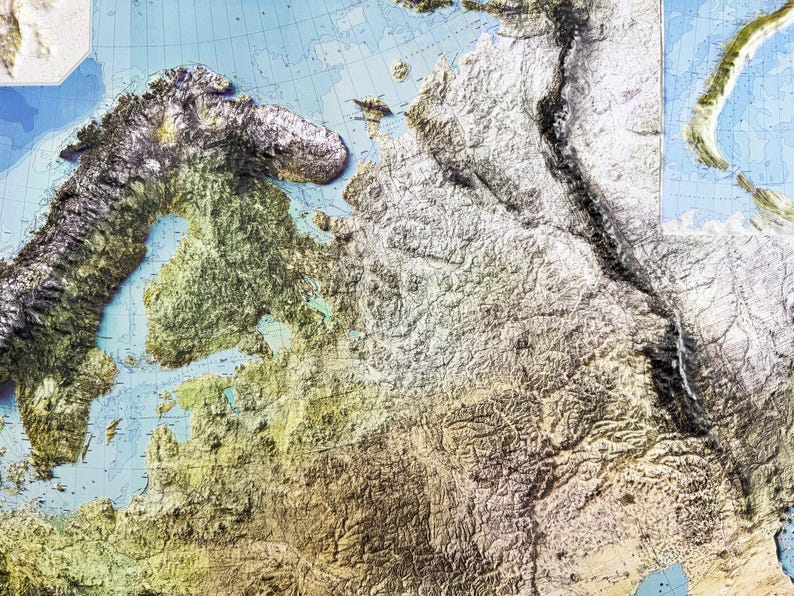 Op de afbeelding: Een gedetailleerde reli&euml;fkaart van Europa, die de gevarieerde topografie van het continent laat zien. De kaart toont tinten groen, bruin en wit, die bergen, vlaktes en wateren vertegenwoordigen. De kaart heeft een blauwe achtergrond met rasterlijnen.