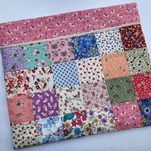 May include: A patchwork zippered pouch featuring a variety of floral and patterned fabrics in pink, blue, green, and purple. The top section is a solid pink with a repeating unicorn pattern. A pink ribbon is attached to the zipper.