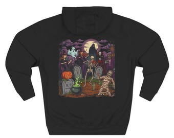 May include: A black hooded sweatshirt featuring a colorful graphic print of a Halloween scene. The illustration depicts a skeleton, a mummy, a ghost, a witch, and a vampire in a graveyard with a bubbling cauldron, a pumpkin, and a full moon.