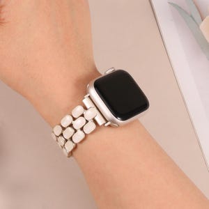 以下が含まれることがあります： 白の楕円形のリンクバンドが付いたシルバーのApple Watch。時計の文字盤は黒で、バンドは一連の接続された丸みを帯びたリンクでできています。時計は手首にあります。