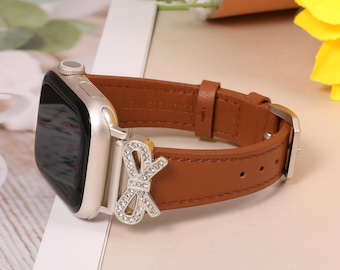 May include: A brown leather watch band with a silver buckle and a silver bow-shaped embellishment encrusted with clear crystals. The watch face is silver with a black screen. The band is made of genuine leather.