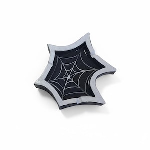 Op de afbeelding: Een stervormige, zwart-witte decoratieve schaal met een spinnenwebontwerp. De schaal heeft een zwart interieur met een zilverkleurig spinnenwebpatroon en een witte rand. De schaal is waarschijnlijk gemaakt van keramiek.