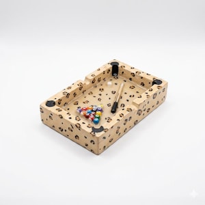 Puede incluir: Un cenicero rectangular con un diseño de estampado de leopardo. El cenicero contiene un juego de bolas de billar en miniatura, un taco y una bola blanca. El cenicero tiene cuatro apoyos de esquina negros.