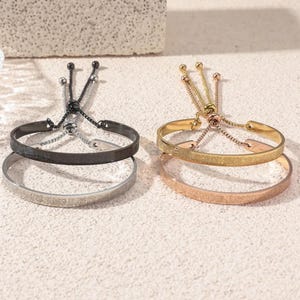 May include: Two sets of adjustable bracelets. One set features a black and silver bracelet, while the other showcases gold and rose gold bracelets. Each bracelet has a delicate chain and ball design for adjusting the size.