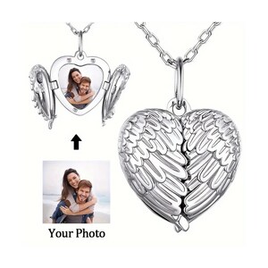 Könnte beinhalten: Eine silberne herzförmige Locket-Halskette mit Flügeldarstellungen. Das Medaillon öffnet sich und zeigt ein Foto. Die Worte "Your Photo" stehen unter einem Foto eines Paares. Die Halskette befindet sich auf weißem Hintergrund.