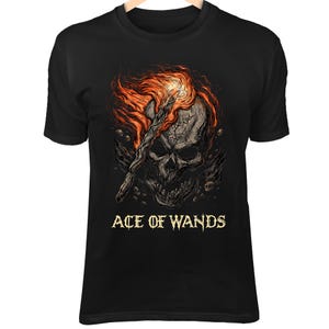 May include: Black t-shirt featuring a detailed illustration of a skull with a flaming wand. The artwork includes fiery orange and red accents, with the text "ACE OF WANDS" in a gold color.