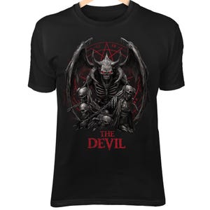 Puede incluir: Camiseta negra con un gráfico detallado de un demonio esquelético con cuernos, alas y ojos rojos, rodeado de calaveras y cadenas. El texto "THE DEVIL" está impreso en rojo en la parte inferior del diseño.