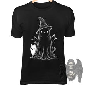 Puede incluir: Una camiseta negra de manga corta con un gráfico de líneas blancas de un gato con sombrero de bruja y capa con alas de murciélago, acompañado de un pequeño gato fantasma. Se muestra un logotipo con una calavera y el texto DARK SHADOW CRAFT.