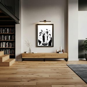 Puede incluir: Una impresión artística en blanco y negro enmarcada, que representa a un grupo de personas reunidas alrededor de una mesa. La obra de arte se exhibe sobre un mueble de madera en un salón moderno. La habitación tiene suelos de madera y una estantería.