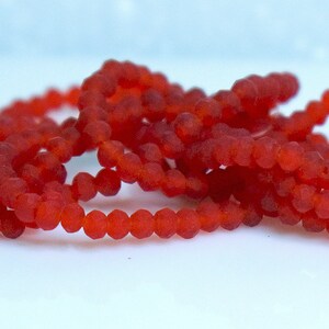 May include: A strand of red glass beads with a frosted finish. The beads are small and round, and they are strung on a clear thread.
