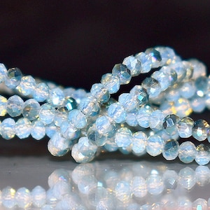 May include: A strand of iridescent blue crystal beads, strung together to form a necklace or bracelet. The beads are faceted and reflect light, creating a shimmering effect.