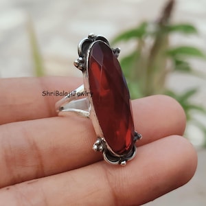 May include: A silver ring featuring a large, faceted, rectangular, deep red gemstone. The ring has decorative silver accents around the gemstone and the band. The text "ShriBalajiJewlry" is visible on the ring.