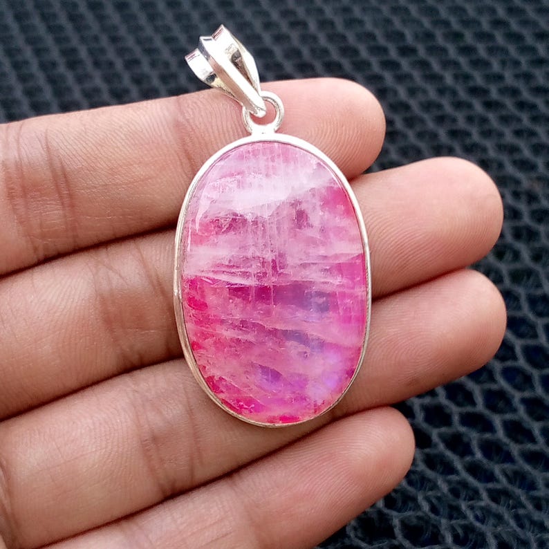 Op de afbeelding: Ovale hanger met een levendige roze edelsteen in een zilverkleurig metalen frame. De edelsteen heeft een gemarmerd uiterlijk met roze en witte tinten. De hanger heeft een lus aan de bovenkant voor een ketting.