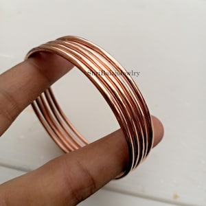 May include: A set of copper-colored bangles. The bangles are round and smooth, with a polished finish. The jewelry is displayed against a light background. The text "ShriBalajiJewlry" is visible in the image.