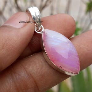 Op de afbeelding: Zilveren hanger met een grote, ovaalvormige, roze en witte edelsteen. De edelsteen heeft een gepolijst oppervlak en is gezet in een zilveren zetting. De hanger heeft een zilveren lus voor een ketting. De tekst "ShriBalajiJewlry" is zichtbaar.