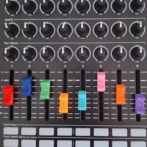 Puede incluir: Controlador MIDI Novation Launch Control XL negro con numerosas perillas, faders y botones. Cuenta con tapas de fader de colores en rojo, azul, verde, naranja, turquesa, rosa y morado. Incluye texto: "LAUNCH CONTROL XL".