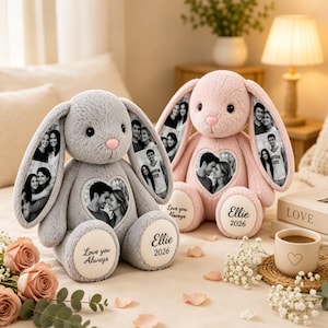 Könnte beinhalten: Zwei Plüschhasen, einer grau und einer rosa, mit individuellen Schwarz-Weiß-Fotodrucken auf den langen Ohren und herzförmigen Brustaufnähern. Die weißen Fußsohlen sind mit dem Namen Ellie, dem Jahr 2026 und dem Text Love you Always bedruckt.