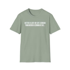 May include: Sage green t-shirt with the text "BETTER A LATE-IN-LIFE LESBIAN THAN NEVER A LESBIAN AT ALL." in white block letters. The shirt has short sleeves and a crew neck. The text is centered on the front of the shirt.