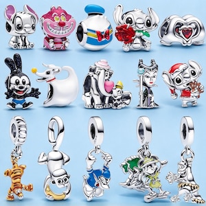 Könnte beinhalten: Eine Sammlung von fünfzehn silberfarbenen Metallanhängern mit verschiedenen Zeichentrickfiguren, darunter Stitch, Donald Duck, Dumbo und Maleficent. Einige Anhänger haben Emaille-Akzente in Rot, Blau, Rosa und Gelb, andere sind mit kleinen Steinen besetzt.