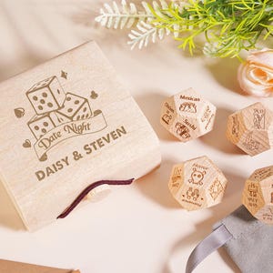 Può includere: Una scatola di legno chiaro con le parole "Date Night" e i nomi "Daisy & Steven" incisi. Accanto alla scatola, quattro dadi di legno con idee per appuntamenti, come "Messicano" e "Guarda un film".