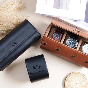 May include: An assortment of watch cases and watch storage, including a black leather roll with the initials "KS", a brown leather watch case holding three watches, and a small black watch case with an antler design.