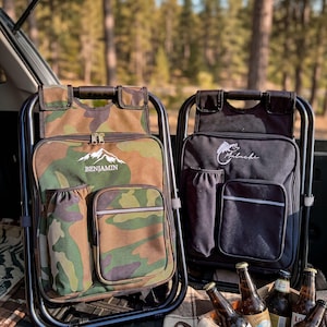 May include: Two folding chair backpacks with black metal frames. One is camouflage print with the text BENJAMIN and a mountain graphic. The other is solid black with a fish graphic and the text Malachi. Both feature side pockets and front pouches.
