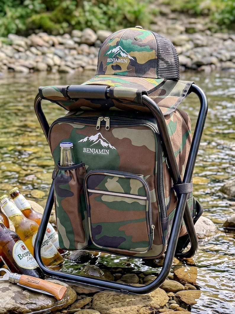 May include: A camouflage print backpack chair with a black metal frame, featuring a matching camouflage baseball cap on top. Both items display a white mountain graphic and the text BENJAMIN. The backpack includes a side pocket holding a glass bottle.
