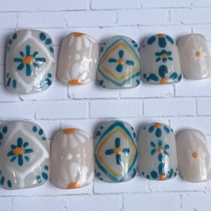 May include: A set of ten press-on nails with a neutral base. Each nail features a unique design, including floral and geometric patterns in teal, yellow, and orange. The nails are arranged in two rows of five.