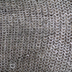 May include: Close-up of a section of chainmail armor. The metal rings are interlocked in a dense pattern, creating a flexible, protective fabric. The silver-colored rings have a slightly weathered appearance.