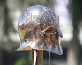 Puede incluir: Un casco plateado pulido con intrincados diseños en relieve. El casco presenta una visera y protectores para las mejillas, y está montado sobre un poste de madera. El casco tiene el texto "FS HANDICRAFTS" en el lateral.