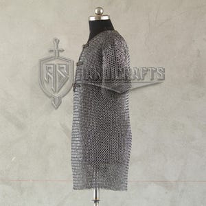 May include: A silver chainmail shirt displayed on a mannequin. The shirt is made of small, interlocking metal rings, creating a flexible, protective garment. The shirt has short sleeves and a straight cut, typical of medieval armor.