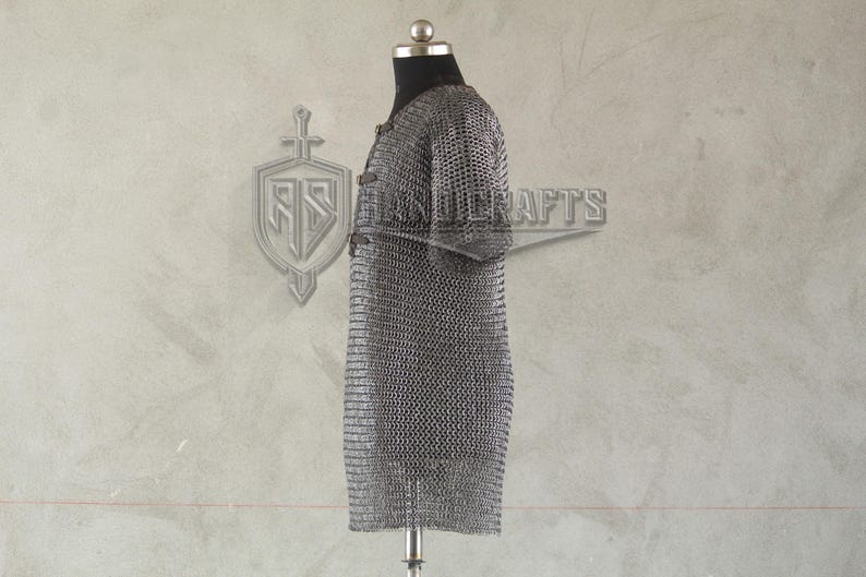 May include: A silver chainmail shirt displayed on a mannequin. The shirt is made of small, interlocking metal rings, creating a flexible, protective garment. The shirt has short sleeves and a straight cut, typical of medieval armor.