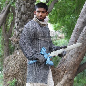 May include: A person wearing a chainmail shirt and holding a wooden sword with a blue hilt. The sword has a light-colored blade. The image is set outdoors with trees in the background. The text "HANDICRAFTS" is visible.