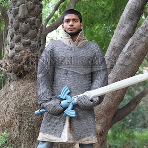 May include: A person wearing a chainmail shirt and holding a wooden sword with a blue hilt. The person is standing in a forest setting. The chainmail shirt is gray and the sword is white. The image has the text "HANDICRAFTS".