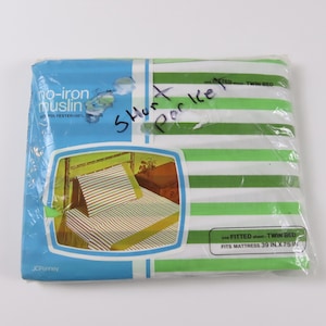May include: A packaged twin bed sheet set with green and white horizontal stripes. The package is labeled "no-iron muslin" and "one fitted sheet". The package also shows a picture of the sheet set on a bed. The package is labeled "JCPenney".