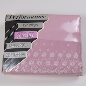 May include: A full-size, no-iron sheet set in a sealed package. The sheets are a light pink colour with a white floral embroidered border. The packaging reads "Performance by Springs" and "Luxury".