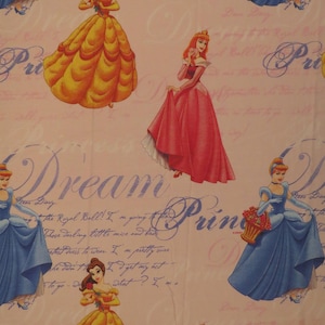 May include: Pale pink fabric with a repeating pattern of Disney princesses in their gowns. The princesses are in yellow, blue, and pink dresses. The background includes script and the words "Dream" and "Princess".